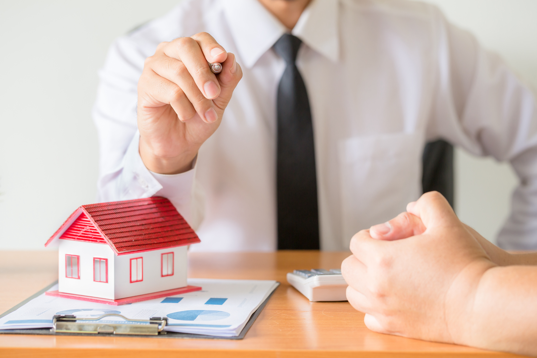 Home salesman stretches holding black pen, model house on wooden desk, Model house with red roof.